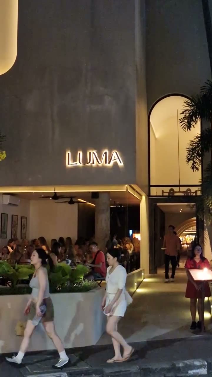 Luma's lit facade on Batu Bolong at night, people passing on the street outside
