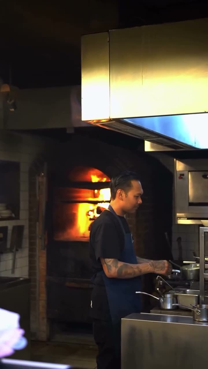A chef working at Luma's see-through wood fire oven, the fire lit behind him