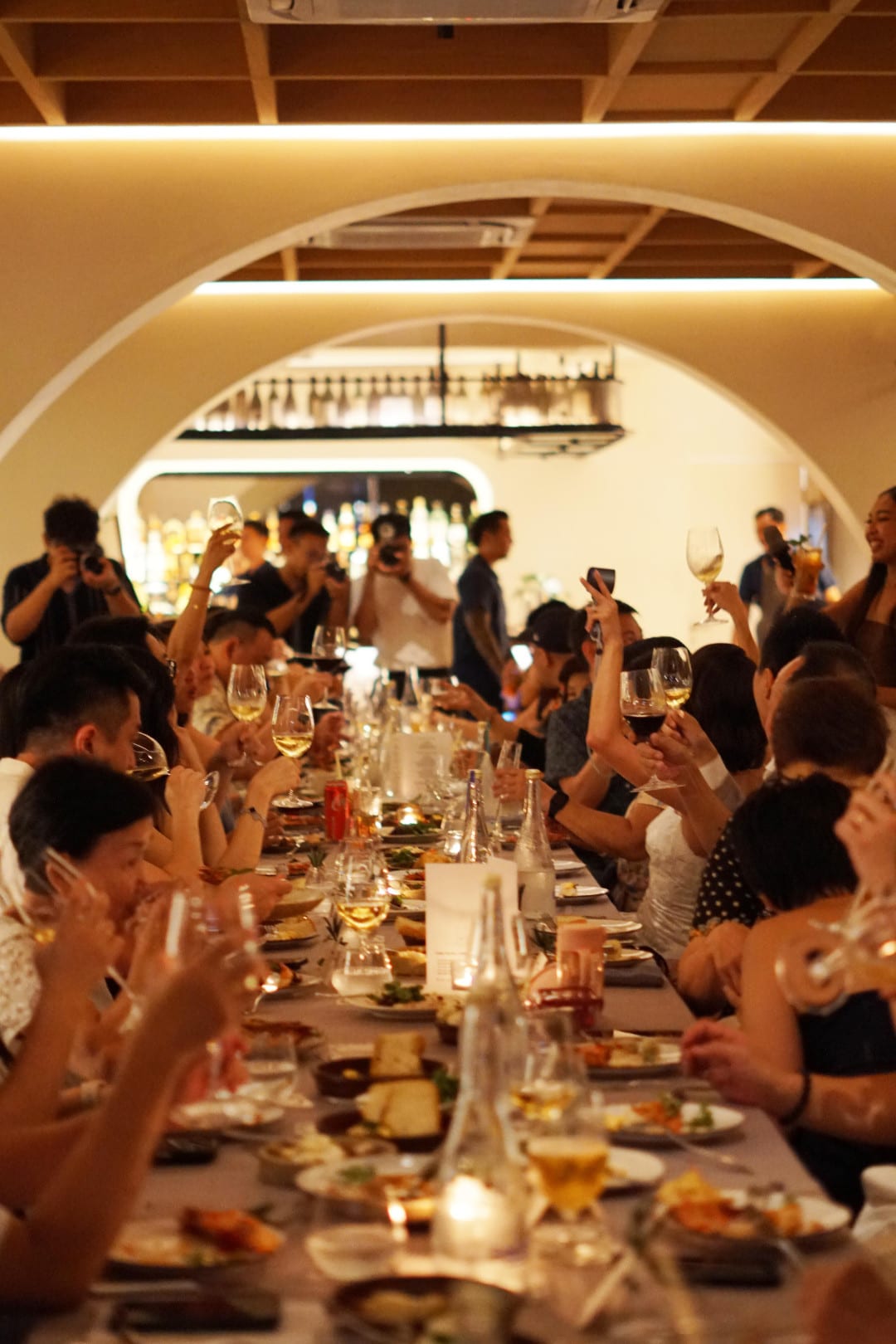 Guests standing to raise their glasses around a long table under Luma's arches