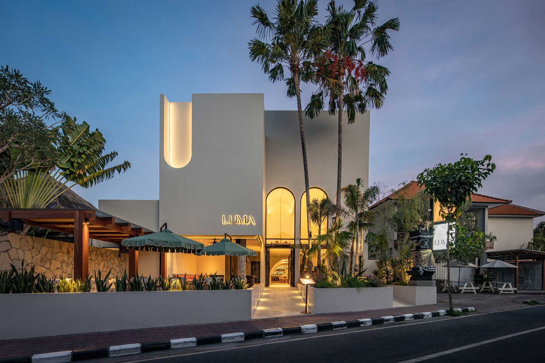 Luma's street elevation at dusk on Jalan Pantai Batu Bolong, the lit LUMA sign above the entrance arch