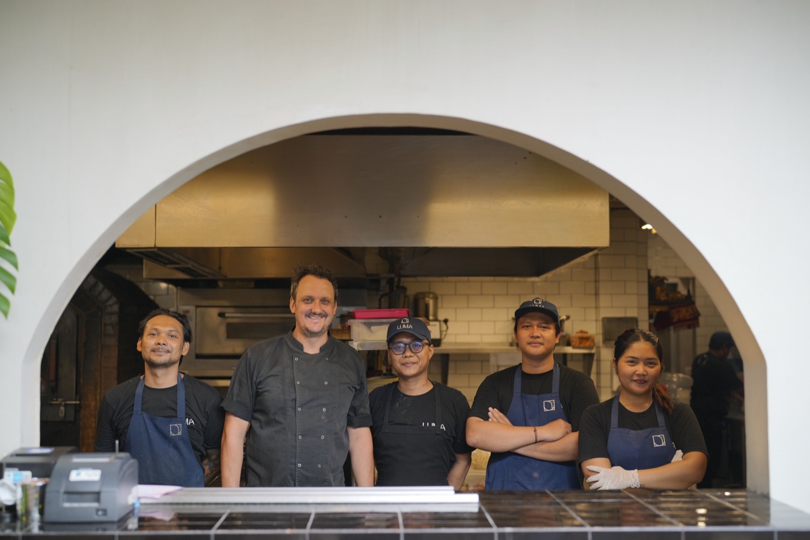 Five of Luma's kitchen team standing at the pass under the arch, the ovens behind them